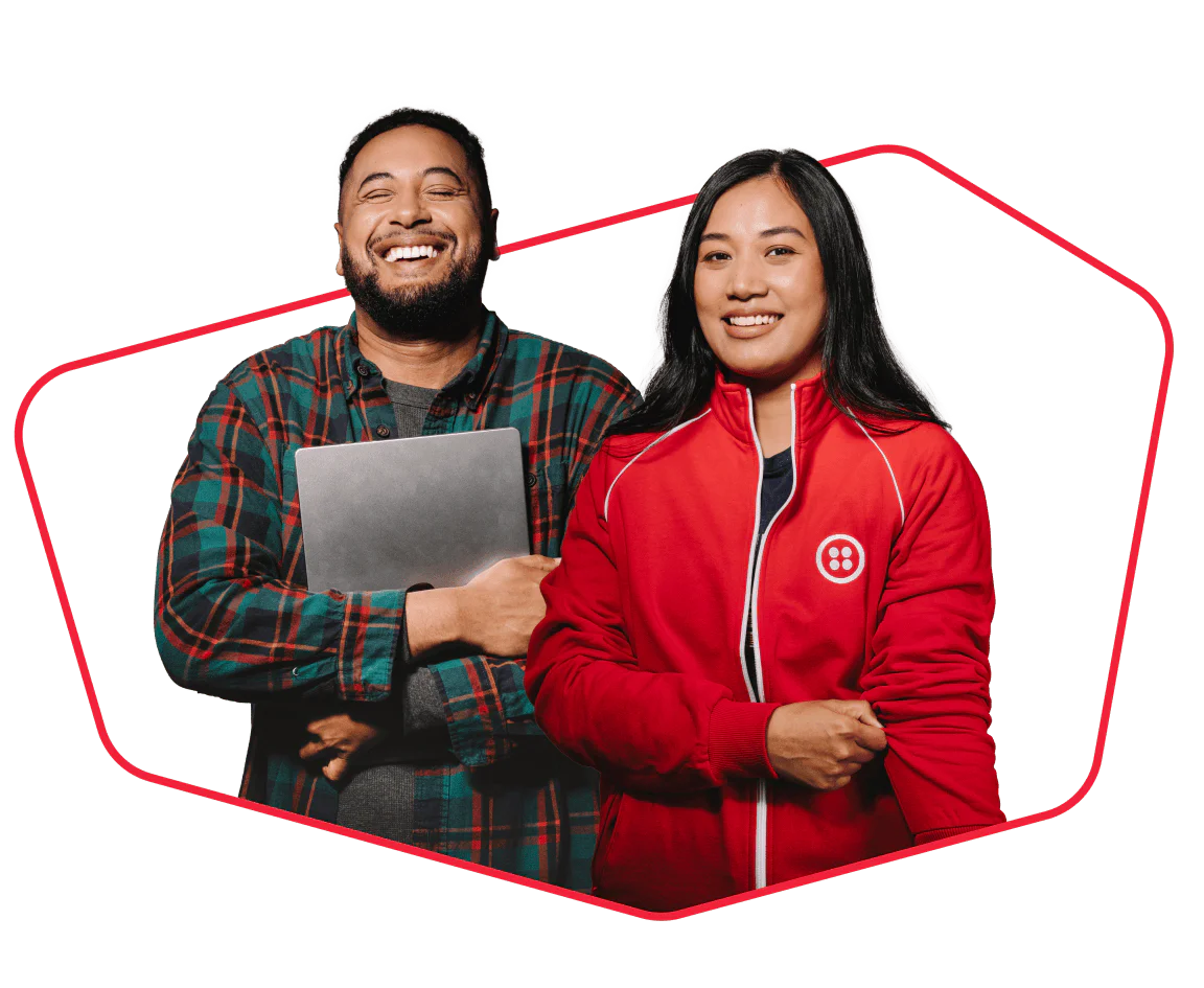 Two happy tech professionals smiling together Two diverse people, one holding a laptop and the other in a red jacket, smiling confidently