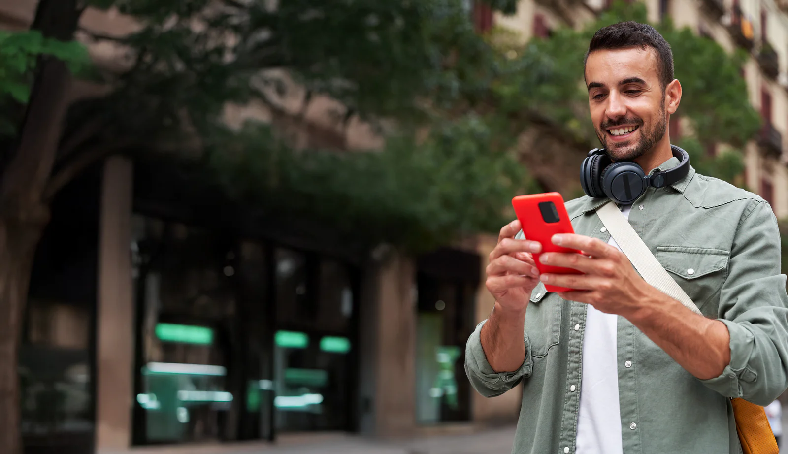 Reliability and transparency are key to consumer trust Young caucasian man holding mobile on the street in the city. Happy male wearing headphones and using cell outdoors, looking and checking his social media. Vertical image with copy space.