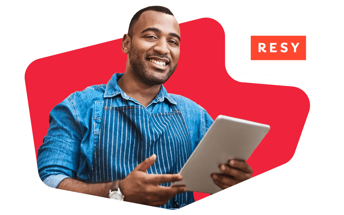 Smiling man using a tablet in a professional setting Man wearing a denim shirt and apron holding a tablet, standing in front of a red background with RESY logo.