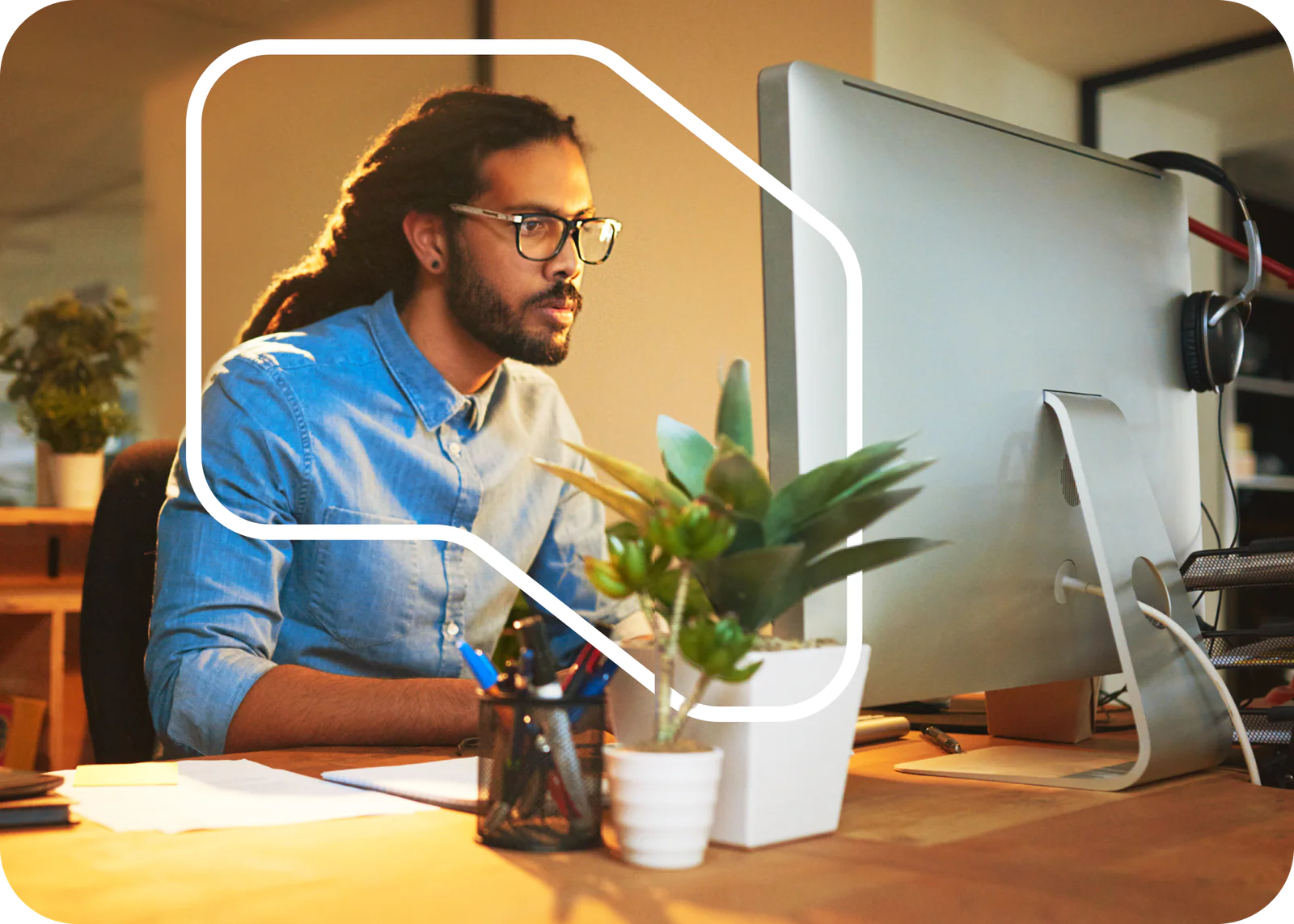 Man with glasses and dreadlocks working at a desktop computer in an office with plants. Man with glasses and dreadlocks working at a desktop computer in an office with plants.