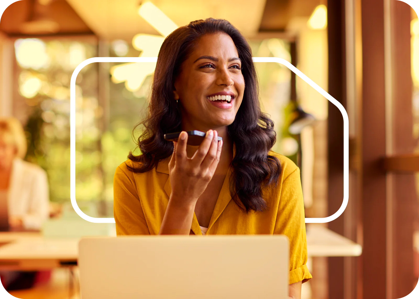 Woman in yellow shirt recording voice message on phone while smiling in a modern office. Woman in yellow shirt recording voice message on phone while smiling in a modern office.
