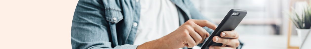 A man wearing a denim shirt using a smartphone, with a blurred background featuring indoor details.