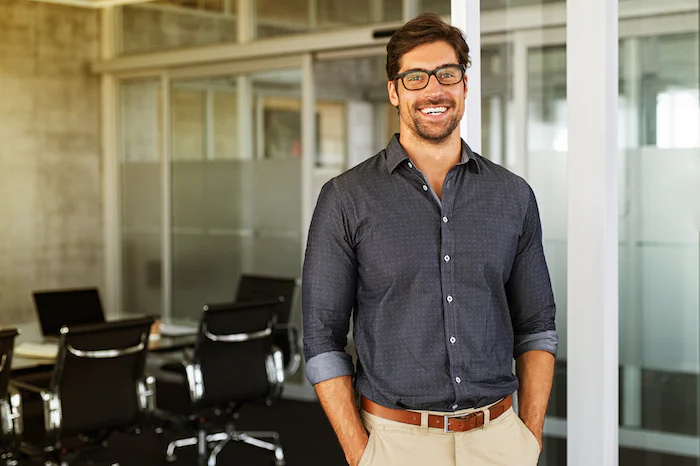 Man in glasses standing and smiling in front of a modern office conference room.