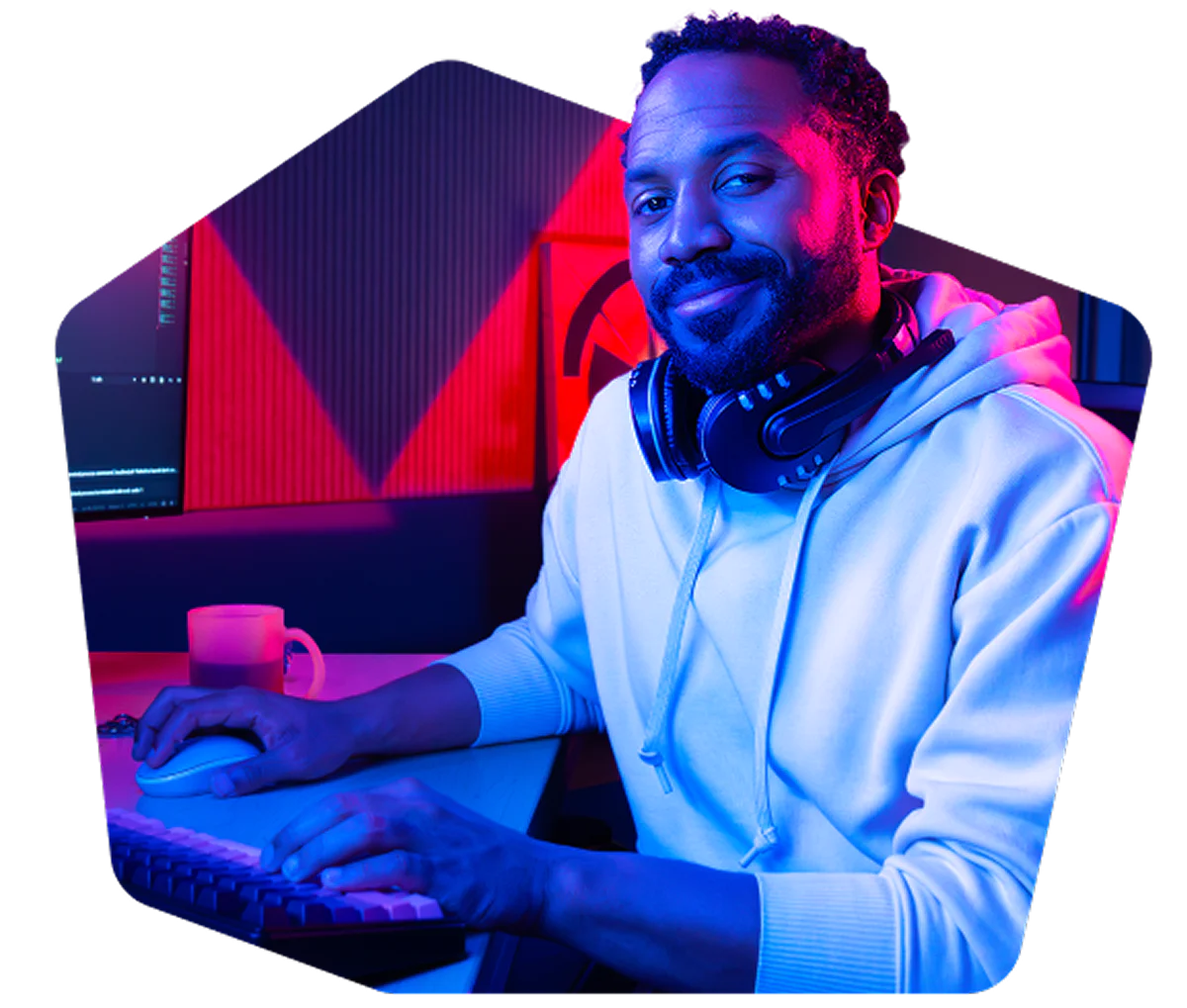 Man at desk with headphones sitting in front of computer in blue and red lighting. Man wearing headphones, sitting in front of a computer, in a room with blue and red lighting.