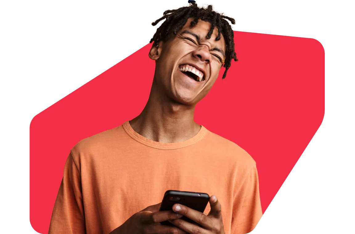 Young Man Laughing While Using Smartphone Smiling young man in an orange shirt holding a smartphone against a red geometric background.