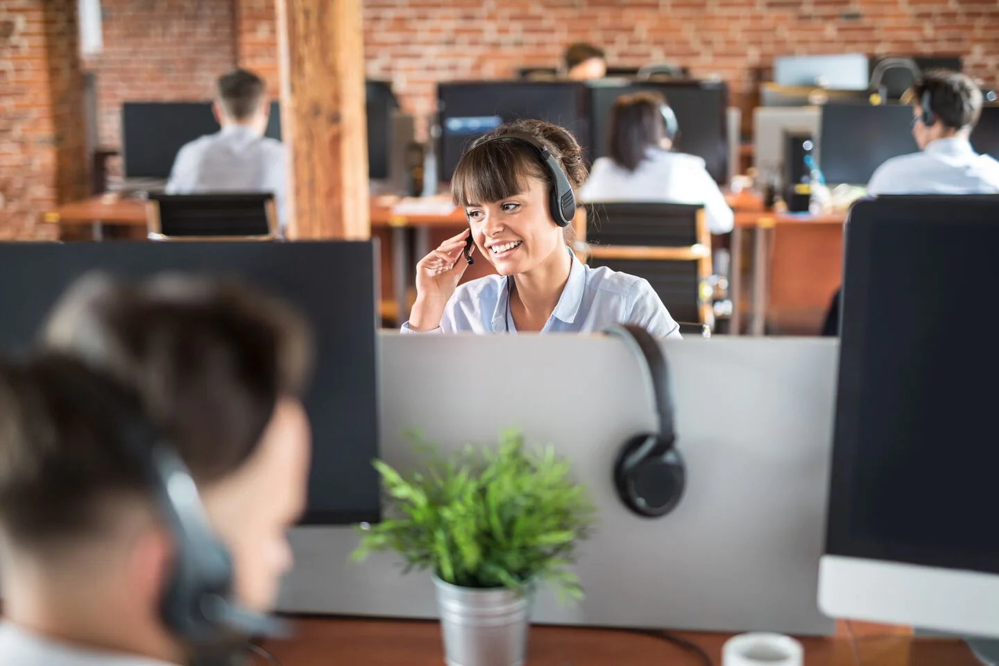 Call Center Employees Working in an Open Office Call center agents wearing headsets, working at desks with computers in a brick-walled open office.