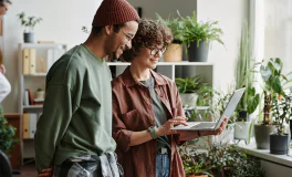 Two people looking at a laptop in a plant-filled office.