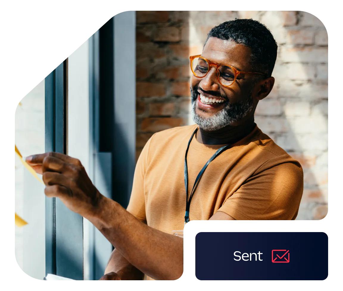 Man smiling while working on a project at a window Smiling man with glasses sticking a note on a window