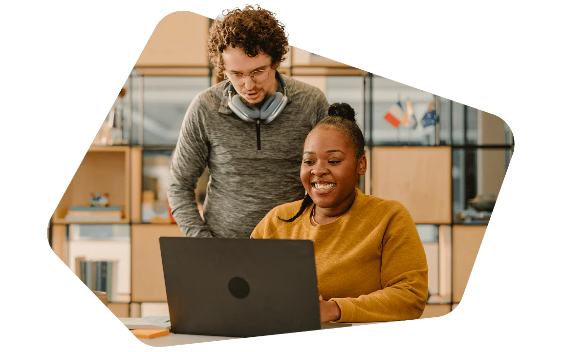 Two colleagues collaborating on a project at the office. Smiling woman working on a laptop with a man standing behind her, both in a modern office.