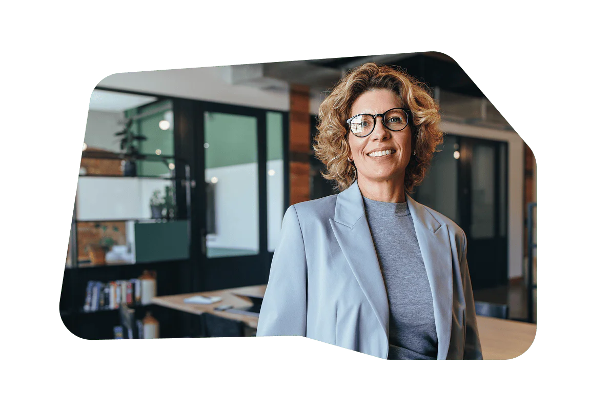 Professional Woman in Modern Office Smiling woman with curly hair and glasses in a blue blazer, standing in a modern office.