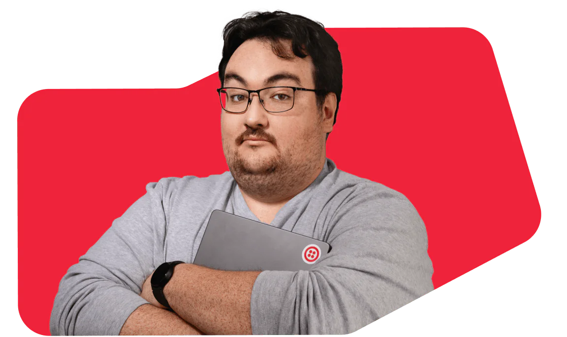Man with Glasses Holding a Laptop Against a Red Background Man wearing glasses and a gray shirt, holding a laptop in a red background