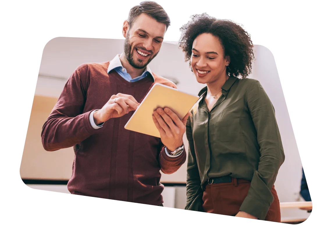 Two colleagues smiling while looking at a tablet together in an office setting.