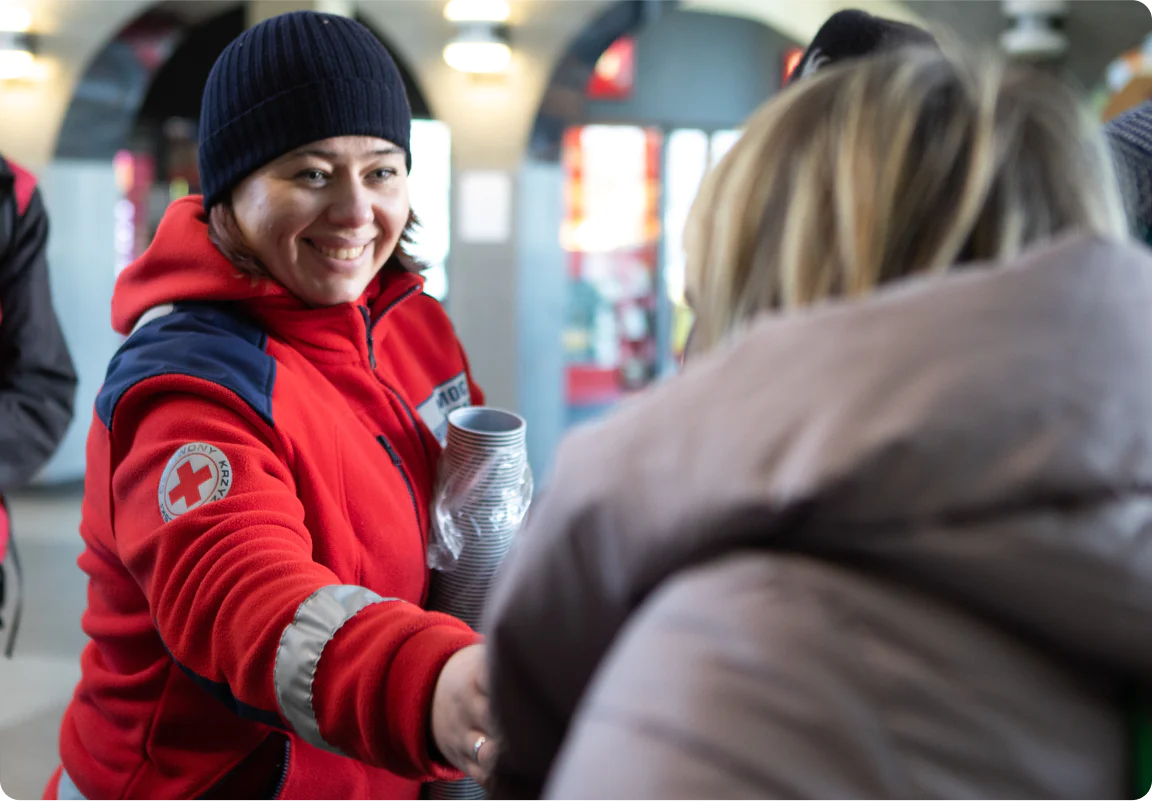 A red cross volunteer providing hot drinks to people in need.