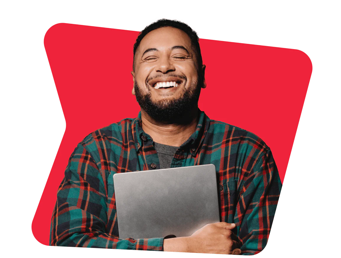 Smiling Man Holding a Laptop Against a Red Background Man in a checkered shirt happily holding a laptop with a red background