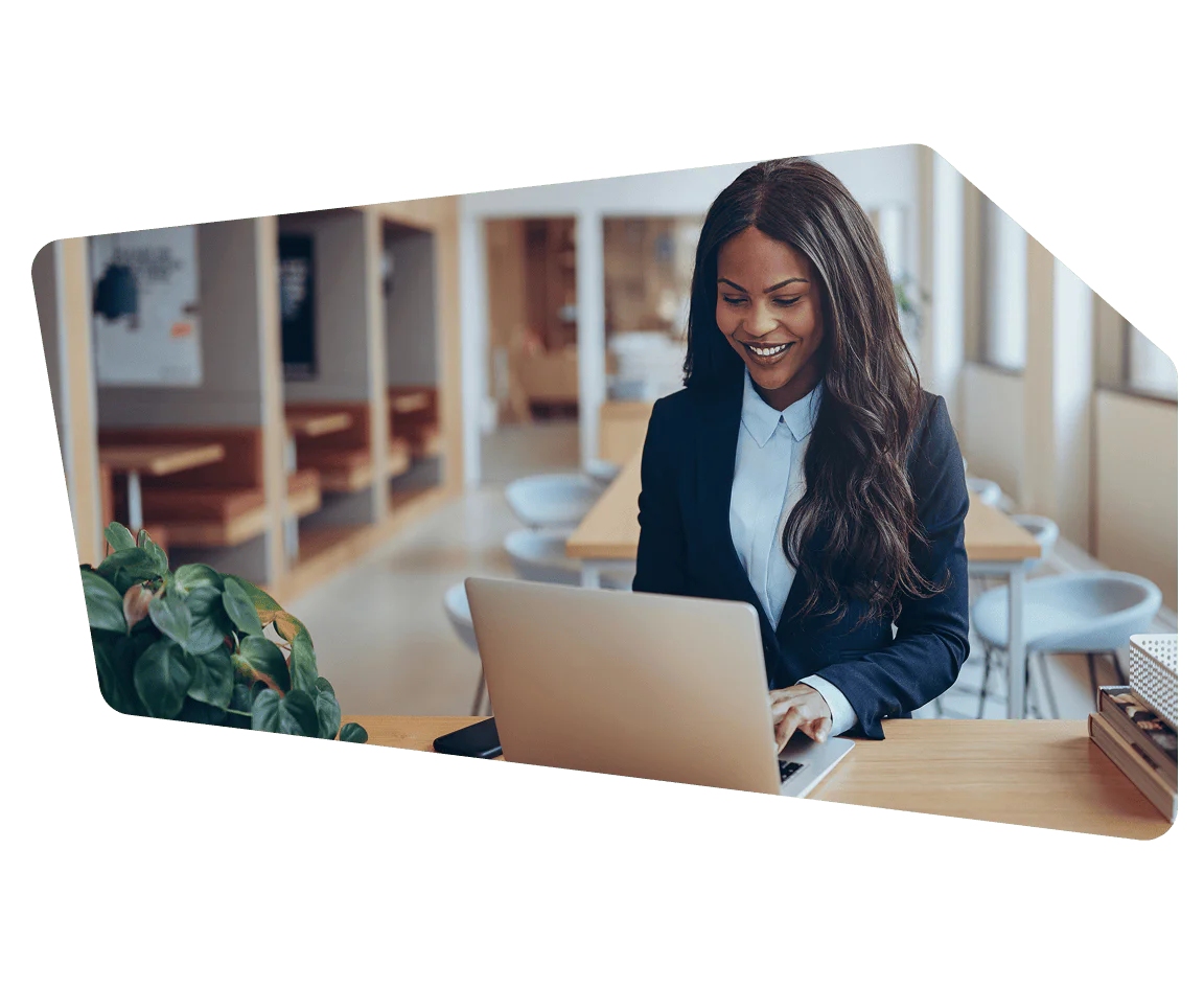 Young Professional Woman Working on Laptop in Modern Office Smiling woman in a business suit using a laptop at a desk in a modern office setting.
